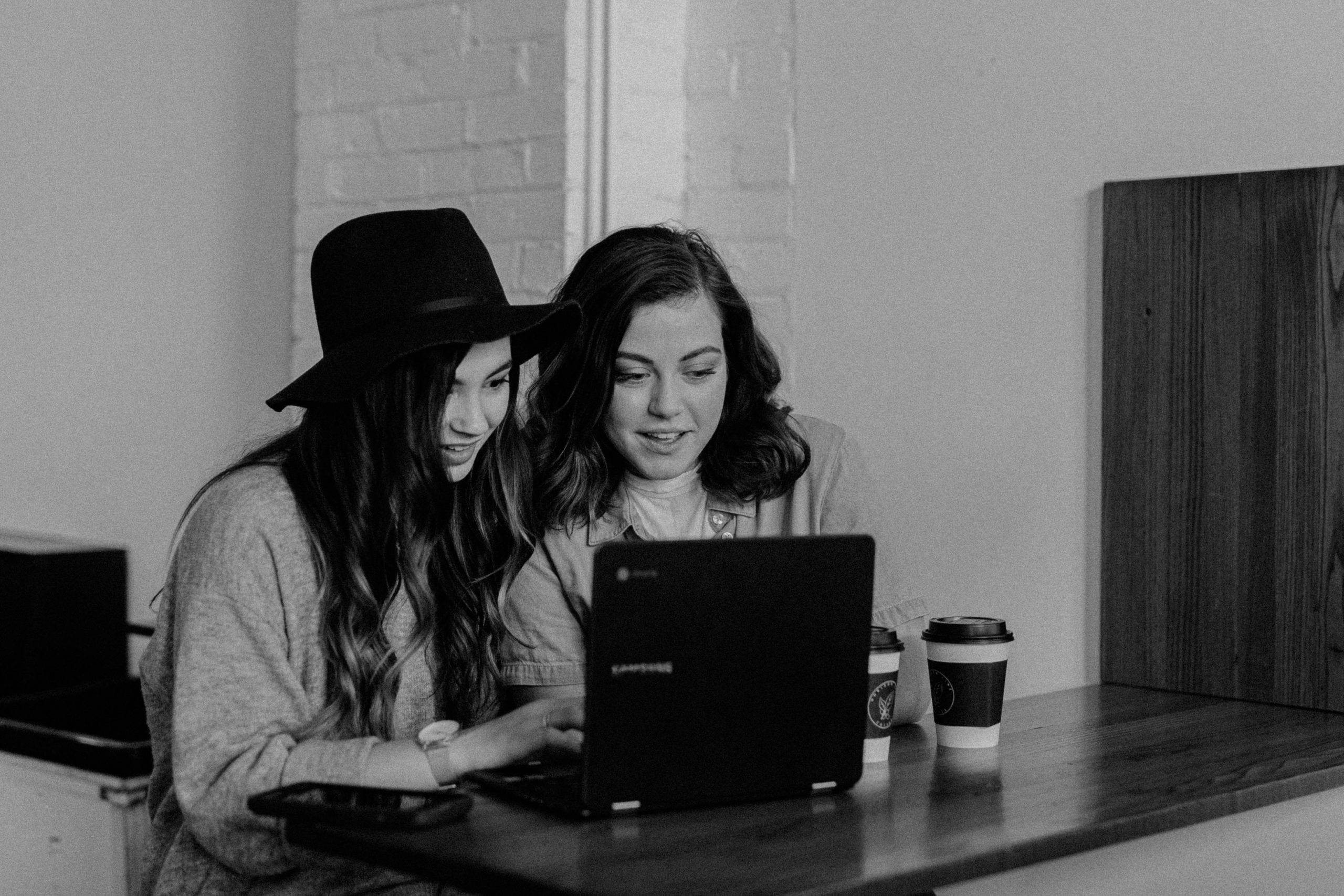 Two women sitting in a cafe, looking at their laptops.