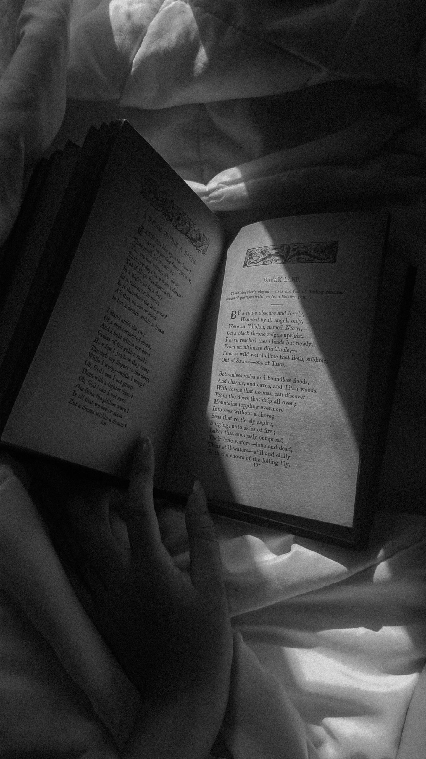 Woman's hand holding a book on her bed.
